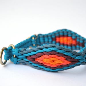 May include: A turquoise and orange dog collar with a woven design. The collar features a brass ring and a pattern of turquoise, gray, orange, and maroon colors. The collar is designed for a pet.