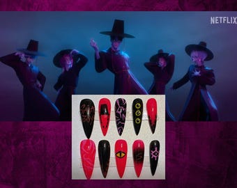 Puede incluir: Un conjunto de diez uñas artificiales largas y puntiagudas con varios diseños. Las uñas presentan colores negro, rojo y rosa con patrones gráficos, incluyendo texto, formas geométricas y un ojo. El fondo muestra una escena de una animación de Netflix.