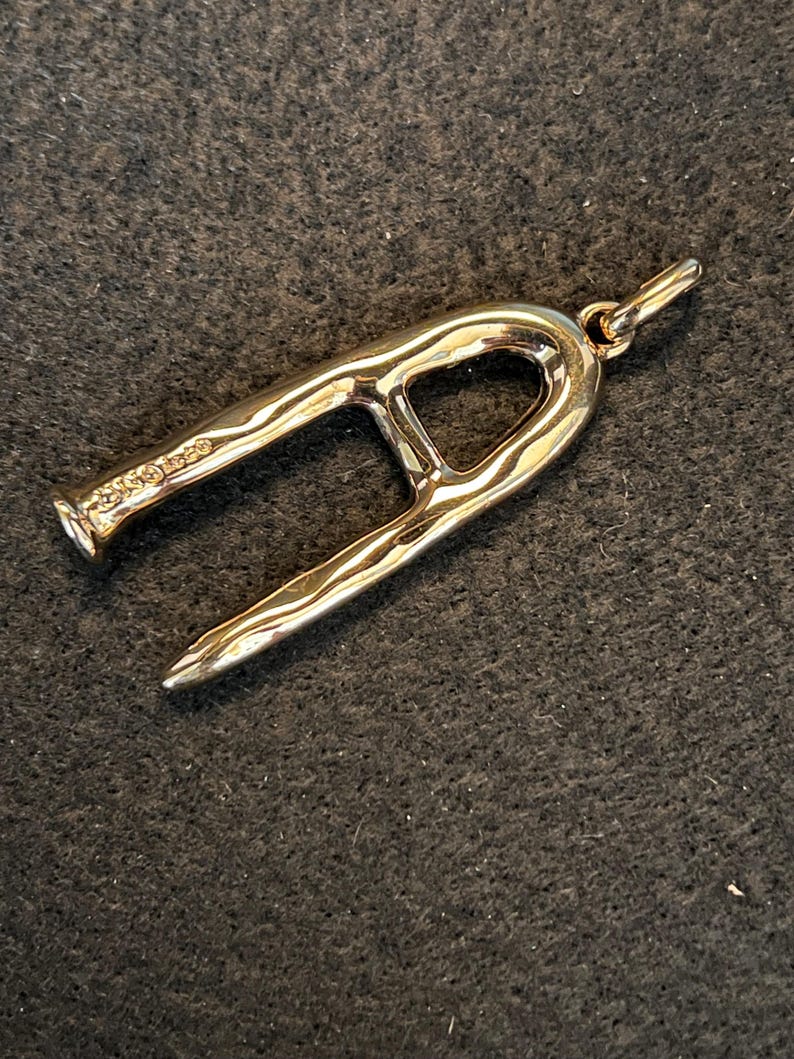 Puede incluir: Un colgante dorado con un dise&ntilde;o abstracto &uacute;nico. El colgante tiene una forma curva y abierta con una superficie texturizada y un peque&ntilde;o lazo para una cadena. El metal tiene un acabado pulido, reflejando la luz.