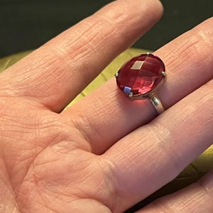 Pode incluir: Anel de prata com uma grande pedra preciosa vermelha rubi oval e facetada. A pedra &eacute; engastada com pequenas garras, e a banda do anel &eacute; de prata polida.