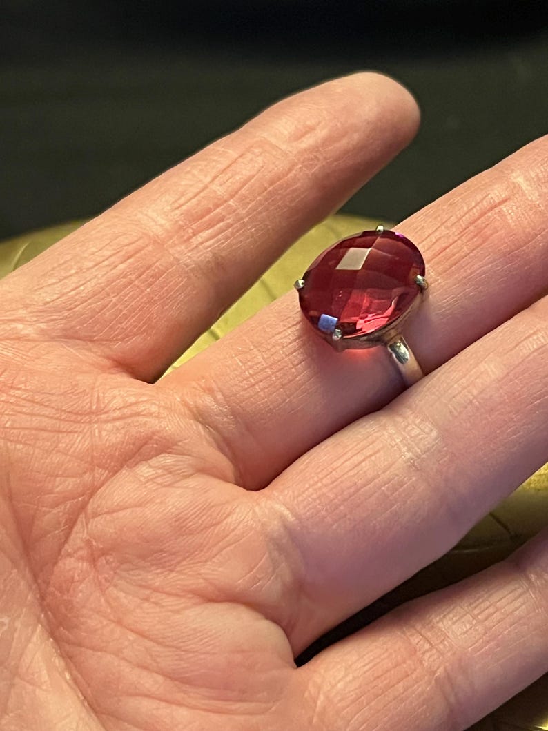 Pode incluir: Anel de prata com uma grande pedra preciosa vermelha rubi oval e facetada. A pedra &eacute; engastada com pequenas garras, e a banda do anel &eacute; de prata polida.
