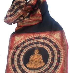 May include: A black and red patterned scarf with a circular design featuring a seated Buddha in the center. The Buddha is depicted in a yellow robe with a halo and is surrounded by concentric circles of red, white, and black.