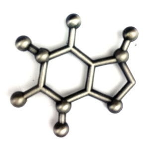 May include: A silver-colored metal model of a caffeine molecule. The model is made up of a series of connected hexagons and pentagons, with small spheres representing the atoms.