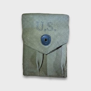 Puede incluir: Bolsa de lona verde oliva con solapa y cierre de botón negro. Las letras "U.S." están estampadas en la parte delantera. La bolsa parece ser vintage o de estilo militar.