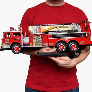 May include: A red toy fire truck with black accents, featuring the text "911" and "55". The truck has a ladder, lights, and a remote control. The words "RESCUE ROOM" and "METRO F.D." are also visible.