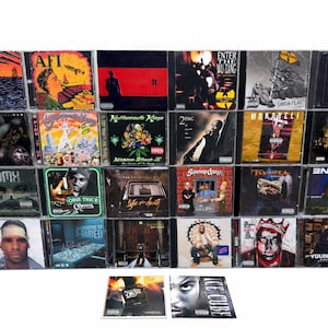 May include: A collection of music CDs featuring various artists and album covers. The covers display diverse artwork, including portraits, abstract designs, and band logos. The CDs are in clear plastic cases, showcasing the album art. Some visible text includes "AFI", "2PAC", and "ICE CUBE".