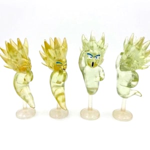 May include: Four translucent yellow figurines of a cartoon character with spiky hair and blue eyes. Each figure is posed differently, mounted on a clear stand. The figures have a ghostly appearance.