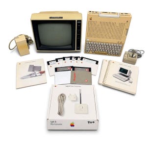 May include: A vintage Apple IIe computer system including a beige monitor, keyboard unit, joystick, and several floppy disks. The set features printed manuals, a box labeled Apple IIe Video Accessories, and various connection cables.