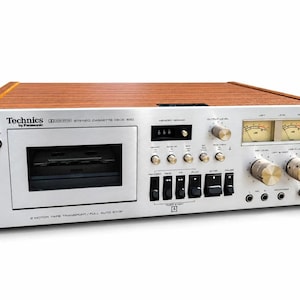 Puede incluir: Una pletina de casete estéreo Technics by Panasonic 650 con panel frontal plateado y paneles laterales con veteado de madera. El dispositivo cuenta con un compartimento para casetes, medidores VU analógicos, perillas, botones y entradas de audio.
