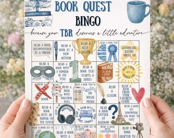 May include: A 2026 Book Quest Bingo card with watercolor illustrations. The card features prompts like "Read a book recommended by a friend" and "Read a book with an animal on the cover." A blue mug and stack of books are also shown.