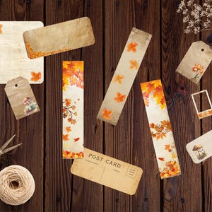 May include: An assortment of autumn-themed stationery, including bookmarks, tags, and a postcard, decorated with fall foliage. The items are arranged on a dark wooden surface, with a ball of twine and scissors.