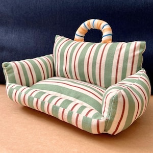May include: A small pet sofa with a green and white striped design, complemented by thin red stripes. It includes a curved handle with orange and blue stripes. The sofa is designed for small pets and has a comfortable, inviting look.