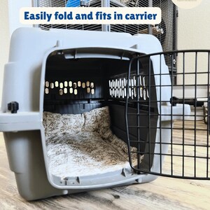 May include: A gray pet carrier with a black metal door is open, revealing a floral patterned bed inside. The text "Easily fold and fits in carrier" is displayed above the carrier. A water bottle is attached to a cage in the background.
