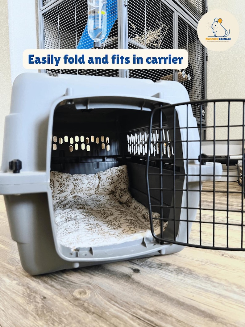 May include: A gray pet carrier with a black metal door is open, revealing a floral patterned bed inside. The text "Easily fold and fits in carrier" is displayed above the carrier. A water bottle is attached to a cage in the background.