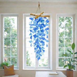 Könnte beinhalten: Ein hängendes Mobile mit zahlreichen durchscheinenden blauen Glasstücken, die an einer Struktur aus natürlichen Holzästen befestigt sind. Die Glassplitter variieren in hellen und dunklen Blautönen und erzeugen an dünnen Schnüren einen Kaskadeneffekt.