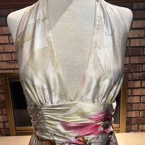 May include: A floral halter-neck dress. The dress has a V-neck and a gathered waist with a band of pink and red flowers. The fabric has a satin sheen. The dress is displayed on a mannequin, and the measurements are in centimetres.