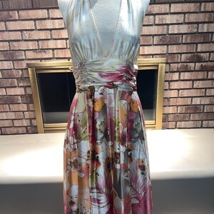May include: A floral print halter dress on a mannequin. The dress has a V-neck, a gathered waist, and a knee-length skirt. The satin fabric displays a pattern of pink, orange, and white flowers. The dress is a vibrant piece.