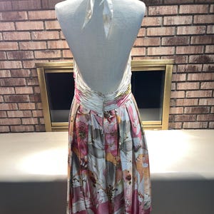 May include: A halter-neck dress with a floral pattern in shades of pink, white, and brown. The dress has a low back and a flowing skirt. The dress is displayed on a mannequin.