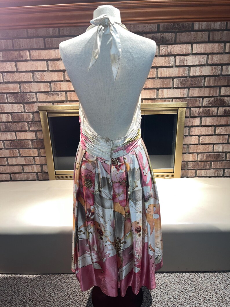 May include: A halter-neck dress with a floral pattern in shades of pink, white, and brown. The dress has a low back and a flowing skirt. The dress is displayed on a mannequin.