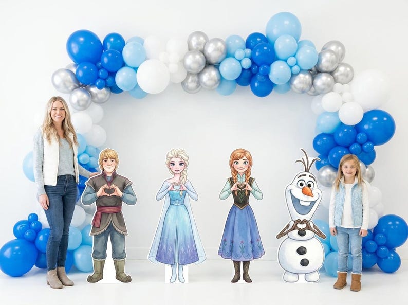 May include: A party scene featuring a balloon arch in shades of blue, silver, and white. Cardboard cutouts of characters from the movie Frozen are displayed in front of the arch, along with a young girl and a woman.