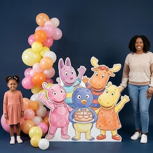 May include: A vibrant party scene with a balloon arch in yellow, orange, and pink. A cardboard cutout of cartoon characters stands next to a young girl and an adult woman. The characters are holding a cake.