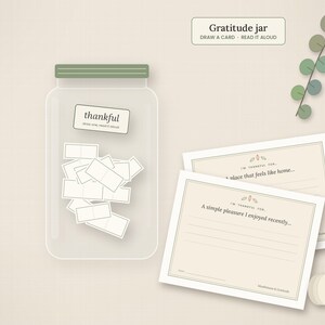 May include: A clear glass gratitude jar with a sage green lid, filled with small white cards. The jar features a label reading thankful. Beside it are two rectangular cards with prompts and a small white pumpkin illustration.