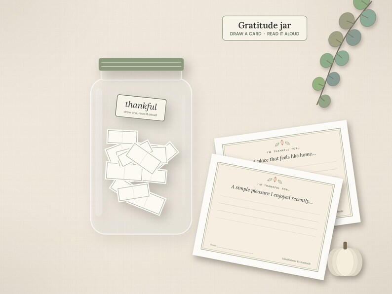 May include: A clear glass gratitude jar with a sage green lid, filled with small white cards. The jar features a label reading thankful. Beside it are two rectangular cards with prompts and a small white pumpkin illustration.