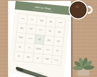 May include: A Self-Care Bingo game sheet with a sage green header, featuring a five-by-five grid of wellness activities and a central free space. The sheet is accompanied by a dark brown coffee mug and a dark green pen on a grid background.