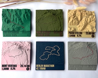 May include: Six square 3D topographical map tiles featuring mountain routes and a marathon course. Colours include green, olive, beige, pink, dark blue, and grey. Each tile displays printed text detailing location names, distances, and elevation stats.