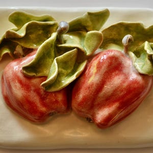 Puede incluir: Dos manzanas de cerámica roja con hojas verdes sobre un fondo blanco.