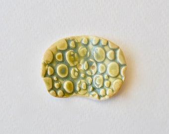 May include: A light green ceramic button with a raised pattern of blue and green circles.