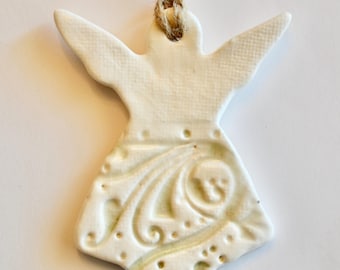 May include: White ceramic angel ornament with a detailed, embossed design. The angel has wings and a flowing gown. It is strung with twine for hanging.