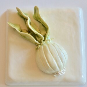 May include: A ceramic sculpture of a white onion with green leaves on a white background.