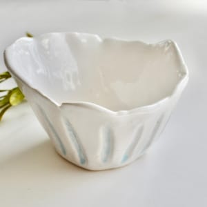 Può includere: Una ciotola in ceramica bianca con un design a coste e strisce blu. La ciotola è fatta a mano e ha una forma unica e organica.