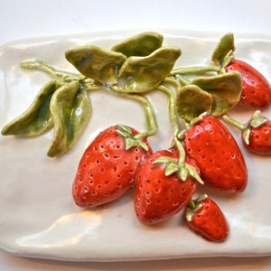 May include: A white ceramic plate with a 3D sculpted design of red strawberries and green leaves.