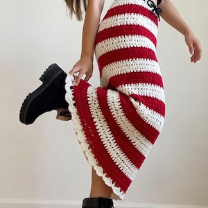 May include: A floor-length crochet skirt featuring horizontal red and white stripes, a drawstring waist, and a scalloped white hem. The skirt is paired with a black sleeveless top and black lace-up boots with thick, lugged rubber soles.