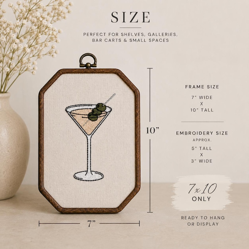 May include: An octagonal wooden frame containing embroidery of a martini glass with two green olives on a pick. The frame measures 7 inches wide by 10 inches tall, while the embroidery measures approximately 5 inches tall by 3 inches wide.