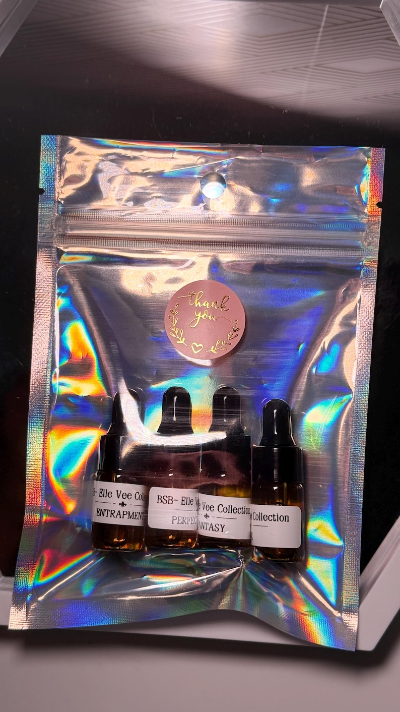 May include: A clear, iridescent pouch containing four small, dark glass bottles with black caps. Each bottle has a white label with text. A pink sticker with the words "thank you" is on the pouch.