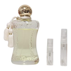 May include: A clear glass perfume bottle with a gold cap and white tassel, accompanied by two small sample spray bottles. The perfume bottle has an ornate design and contains a light yellow liquid.