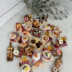 Pode incluir: Miniaturas de alimentos variados, incluindo pastelaria, ovos e frutas, apresentadas em pequenas tábuas de madeira. A cena apresenta guardanapos xadrez vermelhos e brancos, mostrando opções de pequeno-almoço e sobremesa.