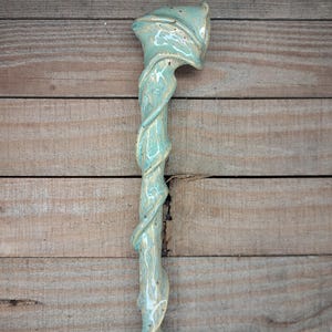 May include: A handcrafted ceramic wand with a turquoise and cream marbled design. The wand features a twisted stem and a flared, textured top. The ceramic wand is a unique decorative item.
