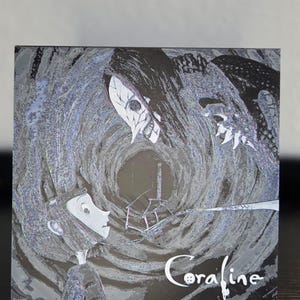 May include: A square artwork in monochrome depicting scenes from the film "Coraline." It shows a girl facing a tall, dark figure with a skull-like mask. The word "Coraline" is written in white script with a button replacing the letter "o."