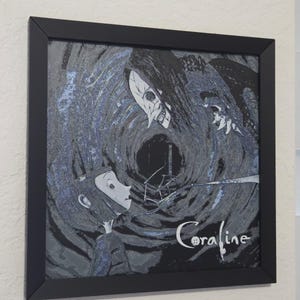 May include: Framed artwork with a stylized illustration from the film "Coraline." The image shows a character confronting a skeletal figure against a dark, swirling backdrop. The title "Coraline" is written in a cursive font.