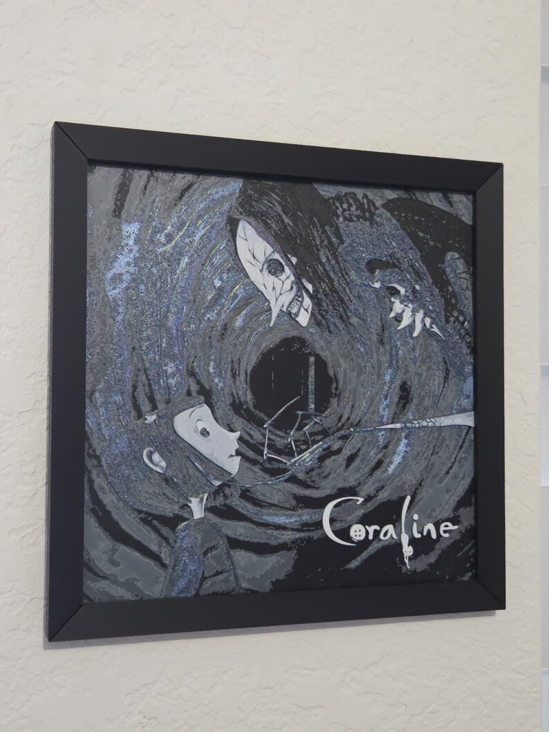 May include: Framed artwork with a stylized illustration from the film "Coraline." The image shows a character confronting a skeletal figure against a dark, swirling backdrop. The title "Coraline" is written in a cursive font.