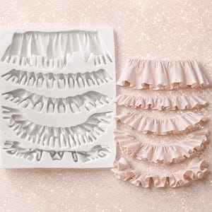 May include: A white rectangular silicone mold featuring five distinct curved channels for creating ruffled shapes, accompanied by five light pink, curved, ruffled fondant or clay pieces that match the shapes within the mold.