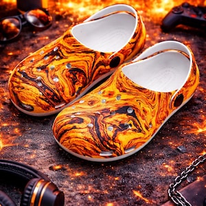 May include: A pair of clogs with a swirling orange and black pattern, resembling lava or fire. The clogs have a white interior and are set on a textured surface. Accessories like headphones, sunglasses, and a game controller are in the background.