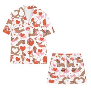 May include: White pyjama set patterned with brown dachshunds, red hearts, and pink balloons. The short-sleeved top and shorts feature a repeating design of the dogs holding balloons and gifts.