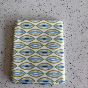 Peut inclure: Tissu plié avec un motif répétitif de formes ovales bleues et vertes sur fond blanc. Le tissu présente un motif de style rétro. Le tissu est probablement en coton ou dans une matière similaire.