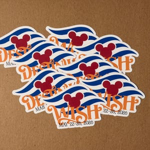 May include: A collection of white stickers with a wave design in blue and white stripes, a red Mickey Mouse head, and the word "WISH" in orange script. The text "DEST" and "MAY 22-26, 2026" are also visible.