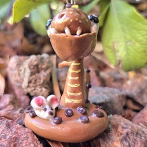 May include: A handmade polymer clay pendant depicting a brown, cartoonish snake with an open mouth and small white teeth. The pendant has a yellow and brown stem and a small mouse at the base. It hangs from a silver-coloured chain.